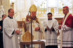 Archbishop Daniel M. Buechlein blesses the episcopal ring, miter and crosier on Feb. 28 that Bishop-designate Christopher J. Coyne, right, would ritually receive during his March 2 ordination at St. John the Evangelist Church in Indianapolis. Assisting the archbishop are Father Patrick Beidelman, left, the archdiocesan director of liturgy, and Ford Cox, second from right, the executive assistant to the archbishop and liaison for episcopal affairs. (Photo by Mary Ann Wyand)