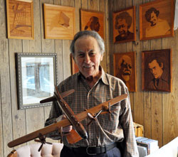 St. Joseph parishioner Robert Foor of Rockville holds a replica of a B-29 airplane that is a World War II souvenir while he stands in front of artwork that he created on wood veneer panels. (Photo by Mary Ann Garber)