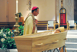 Archbishop Charles C. Thompson spends a quiet moment in prayer by the body of Archbishop Emeritus Daniel M. Buechlein after a Solemn Evening Prayer liturgy on Jan. 30 at SS. Peter and Paul Cathedral in Indianapolis. (Photo by Sean Gallagher)