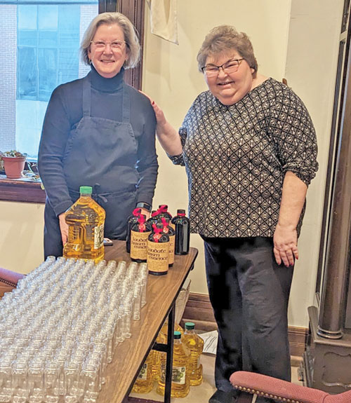 Christina Tuley, right, and Kathy Davis-Shanks of St. Batholomew Parish in Columbus pose in a conference room of SS. Peter and Paul Cathedral Parish’s rectory in Indianapolis on March 20 with the components for assembling the holy oils for the archdiocesan chrism Mass, celebrated on April 26. (Photo by Ann Margaret Lewis)